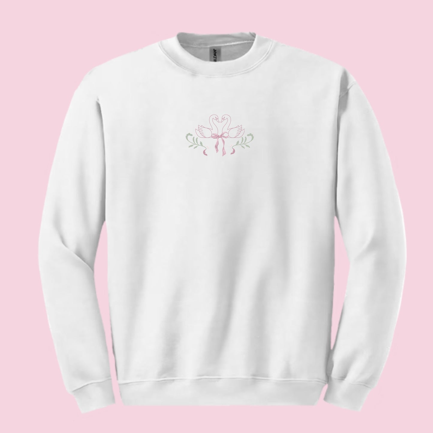 White sweatshirt with a pink and green design featuring a bow and swans on a pink background